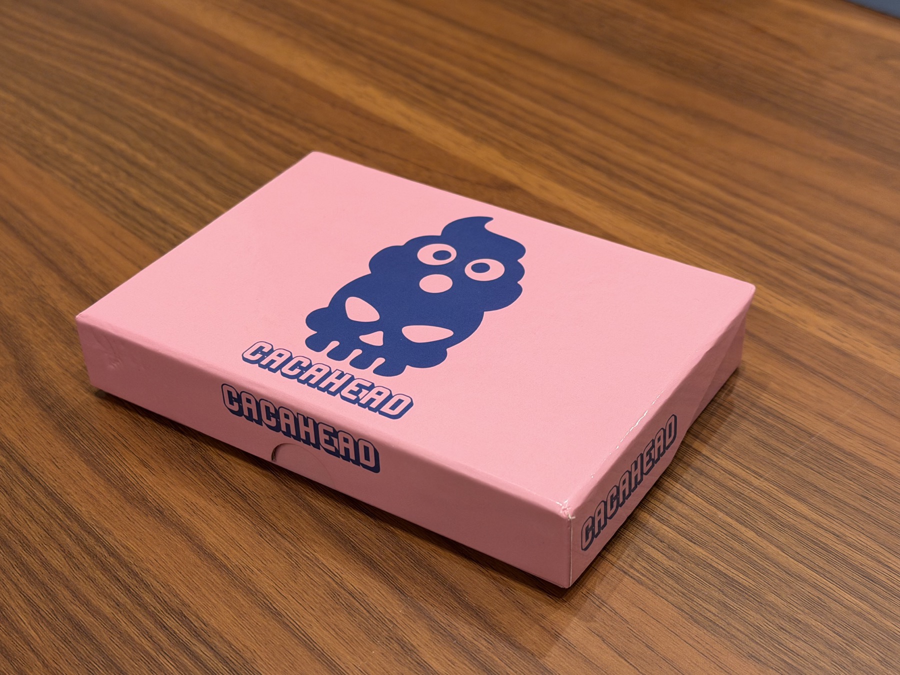 Pink Cacahead card game box on a wooden table